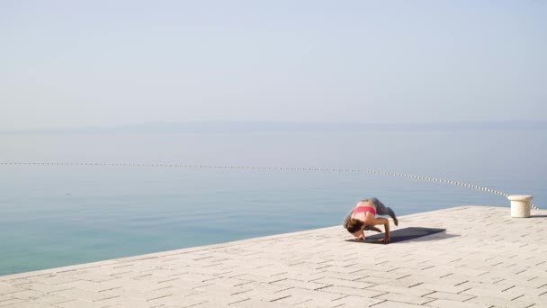 Fit vrouw beoefent yoga op steen bestrating met zee en hemel op de achtergrond — Stockvideo