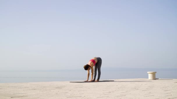 Тренировка йоги взрослой женщиной на пустом причале с морем и небом на заднем плане — стоковое видео