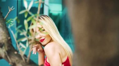 sokakta ağaç dalları arkasında parlak makyaj dansları ile gülümseyen sarışın kadın