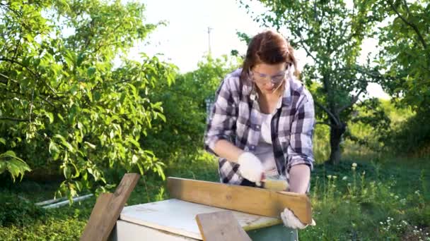 Vrouw timmerman krassen oude houten plank met metalen borstel in zonnige tuin — Stockvideo