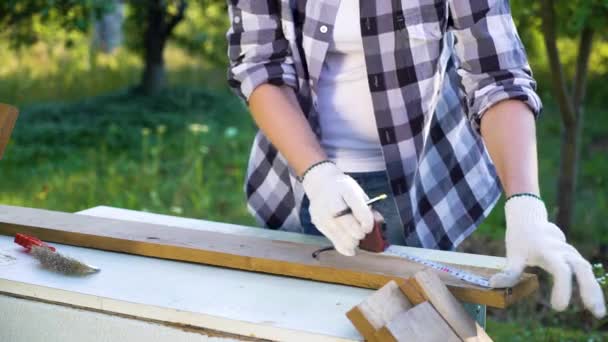 Обрезанный кадр женского плотника измеряет деревянную доску с помощью измерительной ленты — стоковое видео