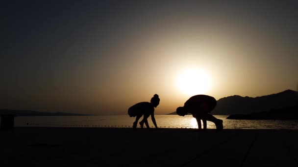 Sziluettje pár csinál jóga a tengerparton napnyugtakor a szabad hely — Stock videók