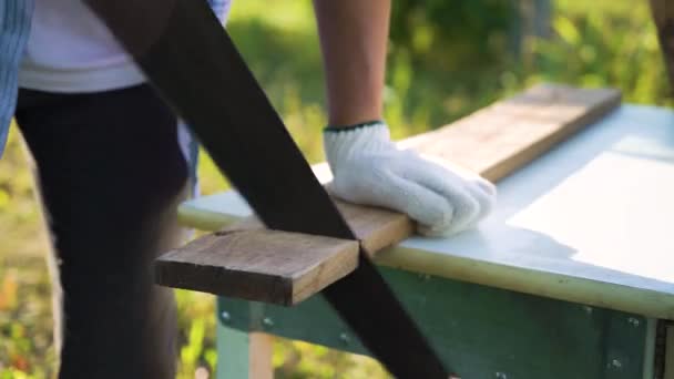 Mains de charpentier en gros plan dans des gants de protection coupant la planche en bois avec la scie à main — Video