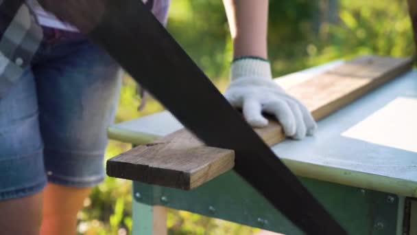 Close-up weibliche Hände in Schutzhandschuhen sägen Holzplanke draußen — Stockvideo