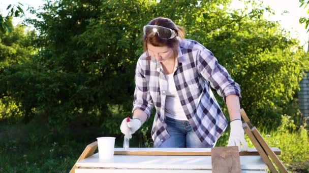 Mujer pintando tablones de madera con pintura blanca en huerto de verano — Vídeo de stock