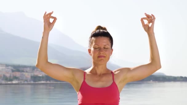 Arc shot of adult woman closed her eyes practicing yoga at mediterranean seaside — Stock Video