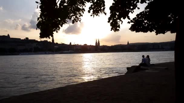 Silhouette eines jungen Paares, das auf der Seebrücke sitzt und bei Sonnenuntergang Wein trinkt — Stockvideo