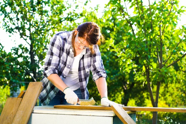 Woman carpenter sanding old wooden plank with metal brush in backyard — Stock Photo, Image