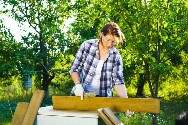 crafts woman in protective glasses and gloves doing woodwork in summer garden