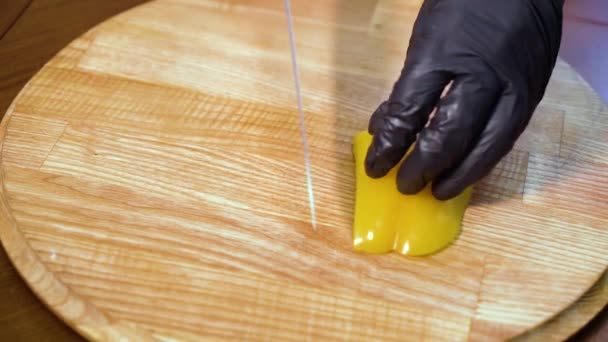 Gros plan de mains de chef en gants coupant le poivron jaune en tranches sur la planche à découper — Video