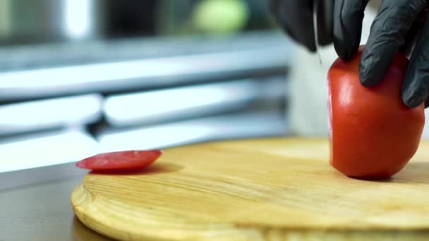 Panoramische Nahaufnahme von Küchenhänden in Handschuhen, die Tomaten auf einem Holzschneidebrett schneiden — Stockvideo