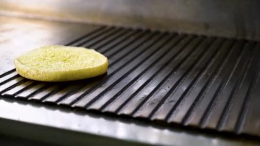closeup şef el sıcak ızgara üzerinde burger çörekler koyar ve tereyağı ile gresler