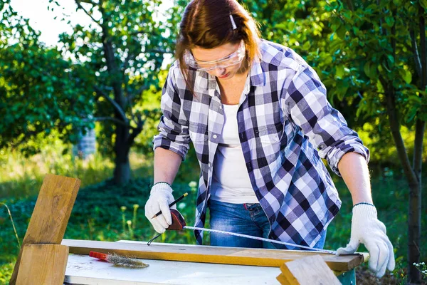 güvenlik gözlüklerinde kadın marangoz ölçüm bandı ile ahşap tahta ölçer