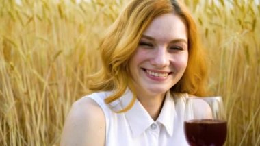 mutlu kadın portre kamera bakarak ve buğday alanında şarap içme