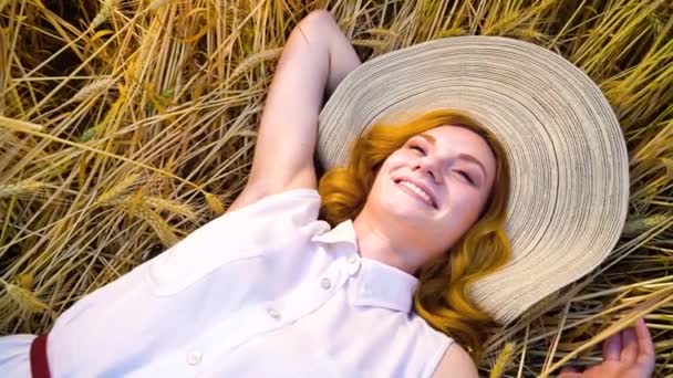 Arriba ver joven romántica mujer pelirroja acostada en el campo de trigo y soñando día — Vídeos de Stock