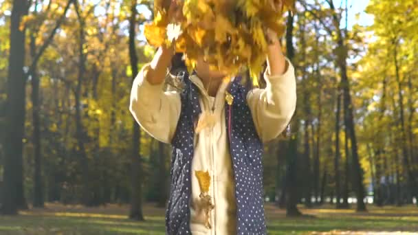 Cheerful little girl throws autumn leaves in front of camera in slow motion — Stock Video