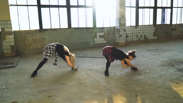 Tiro de arco de dos bailarinas que se extienden en el pasillo de la vieja fábrica con destello de lente — Vídeos de Stock