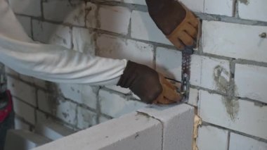 duvar ait birleştirme kelepçesini düzeltmek için vidaları çekiçleyen eldivenlerde inşaatçı elleri