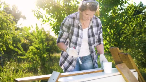 Lens flare on woman in ckecked shirt painting wooden plank with white paint — Stock Video