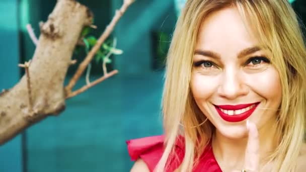 Portret van charmante blonde dame in het rood kijkend naar camera en dansen buiten — Stockvideo