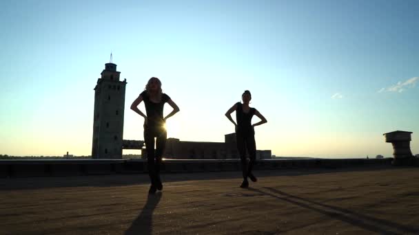 Lente destello en las mujeres en trajes de cuerpo bailando en el techo al atardecer — Vídeos de Stock