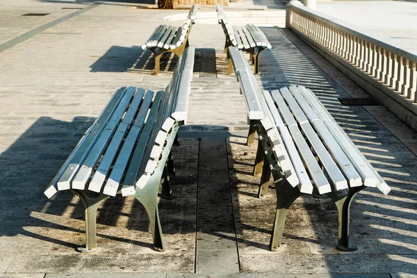 Ranní sluníčko na několika bílých lavičkách na chodníku — Stock fotografie