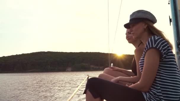 Вид збоку на двох лесбійок, що тримають руки на вітрильному човні і спостерігають за заходом сонця — стокове відео