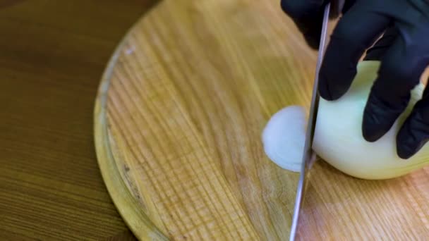 Closeup pan shot of chef hands in gloves chopping onion on wooden cutting board — Stock Video