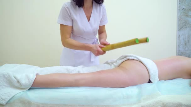 Female masseur doing massage with bamboo sticks on woman buttocks and thighs — Stock Video