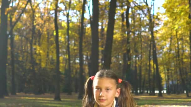 Ζεστό φως του φθινοπώρου σε χαριτωμένο μικρό κορίτσι ρίχνοντας κίτρινα φύλλα στην κάμερα — Αρχείο Βίντεο