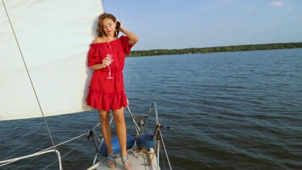 Şarap bardağı ile yelkenli teknede duran kırmızı elbiseli kadın — Stok video