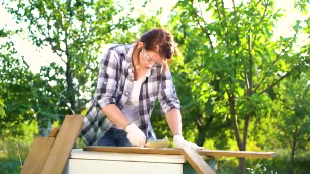 Sunshine op vrouwelijke timmerman krassen oude houten plank met metalen borstel — Stockvideo