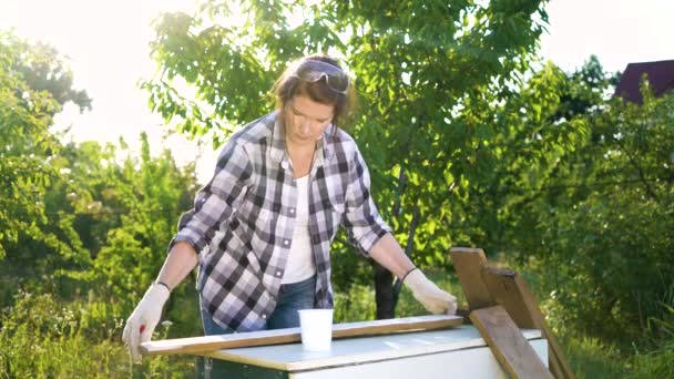 Sunshine on crafts woman painting wooden plank with white paint in backyard — Stock Video