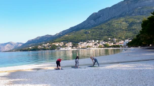 Three women stretch during yoga class on beautiful adriatic seaside in morning — Stock Video