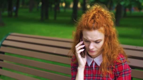 Triste menina de cabelos vermelhos falando no telefone no parque — Vídeo de Stock