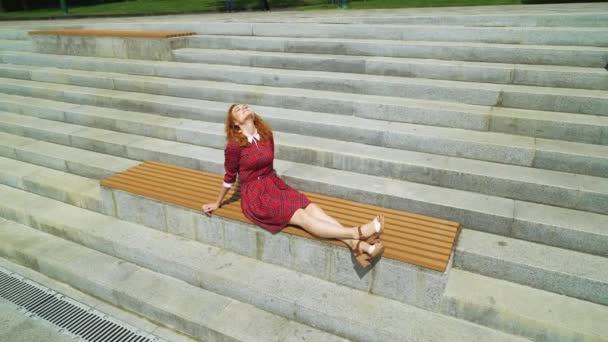 Heureuse fille aux cheveux rouges profitant du temps chaud dans le parc — Video