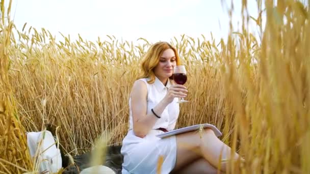 Hübsche rothaarige Mädchen beim Picknick mit Wein im Weizenfeld — Stockvideo