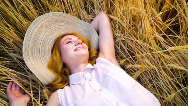 Летом на пшеничном поле лежит улыбающаяся позитивная девушка — стоковое видео