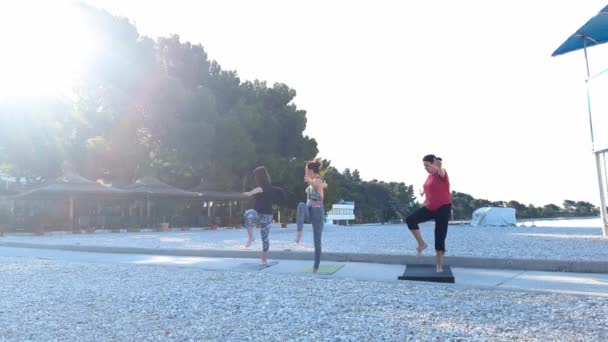 Tre donne che fanno yoga sulla spiaggia di mare vuota al mattino con effetto bagliore lente — Video Stock