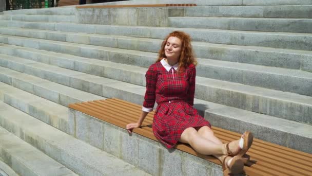 Rozkošná rudovlasá dívka relaxační na lavičce v parku — Stock video