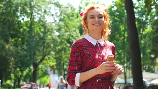 Mignon fille aux cheveux rouges manger de la crème glacée dans le parc le jour ensoleillé — Video