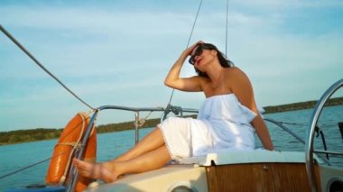 Beyaz elbiseli pozitif kadın yelkenli teknede yaz tatilinin tadını çıkarıyor