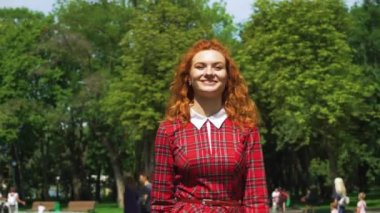 Güneşli bir günde yeşil parkta yürüyen neşeli kırmızı saçlı kız