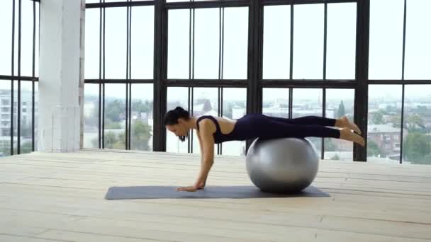 Молодая женщина делает упражнения с фитнес-мячом в студии — стоковое видео