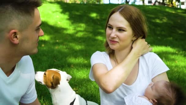 Щаслива сім'я сидить на зеленому газоні з дитиною і домашнім улюбленцем — стокове відео