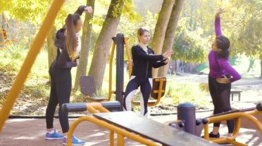 Çeşitli sporcu grupları güneşli bir günde spor sahasında esniyorlar.