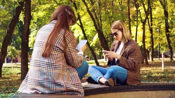 Hipster niñas surfeando en las redes sociales en los teléfonos inteligentes al aire libre — Vídeo de stock