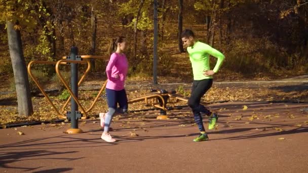Fiatal pár bemelegítés a sportpályán az őszi parkban — Stock videók