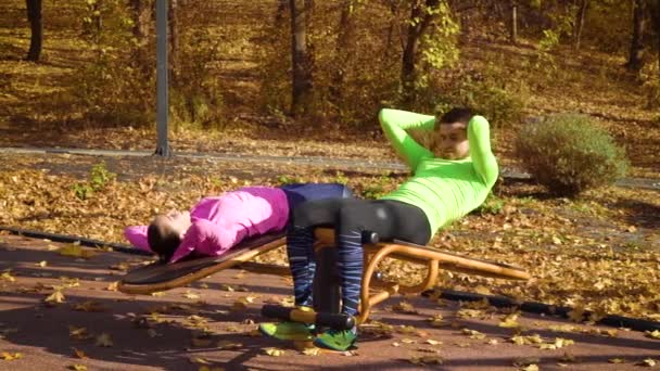 Mladý pár dělá břišní cvičení na sportovním hřišti v podzimním parku — Stock video