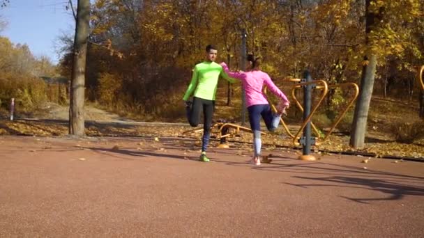 Спортивна пара розтягує ноги на спортивному майданчику пара в сонячний день — стокове відео